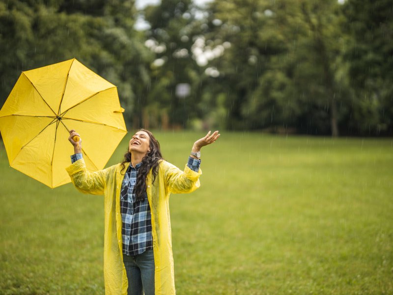 Frau, die mit einem gelben Regenschirm auf einer verregneten Wiese steht