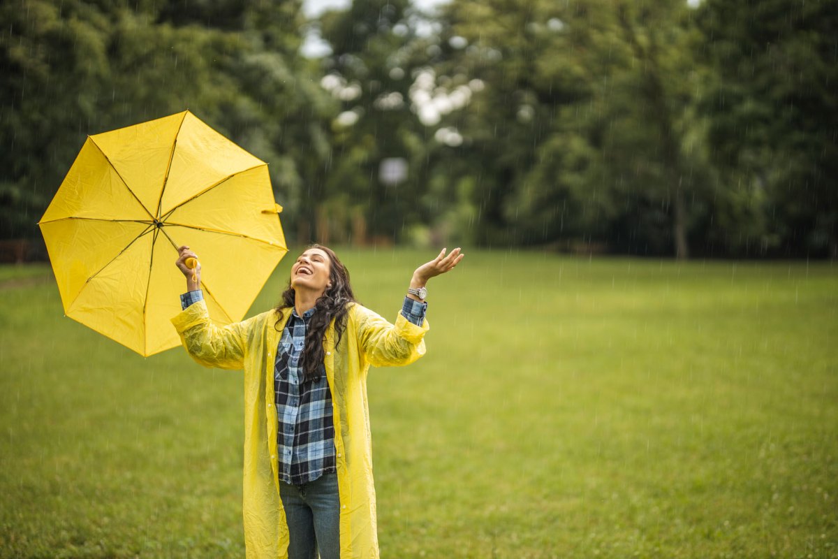 Frau, die mit einem gelben Regenschirm auf einer verregneten Wiese steht