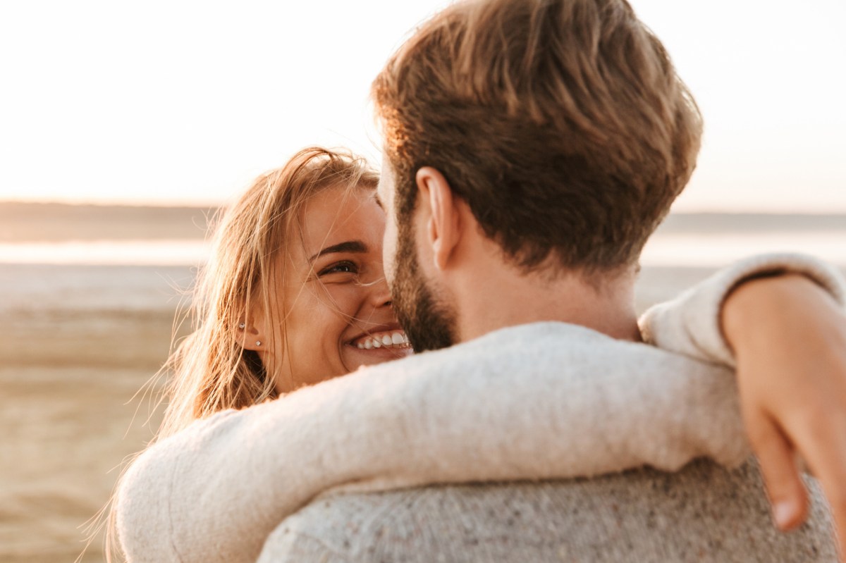 Frau und Mann liegen sich in den Armen am Strand.