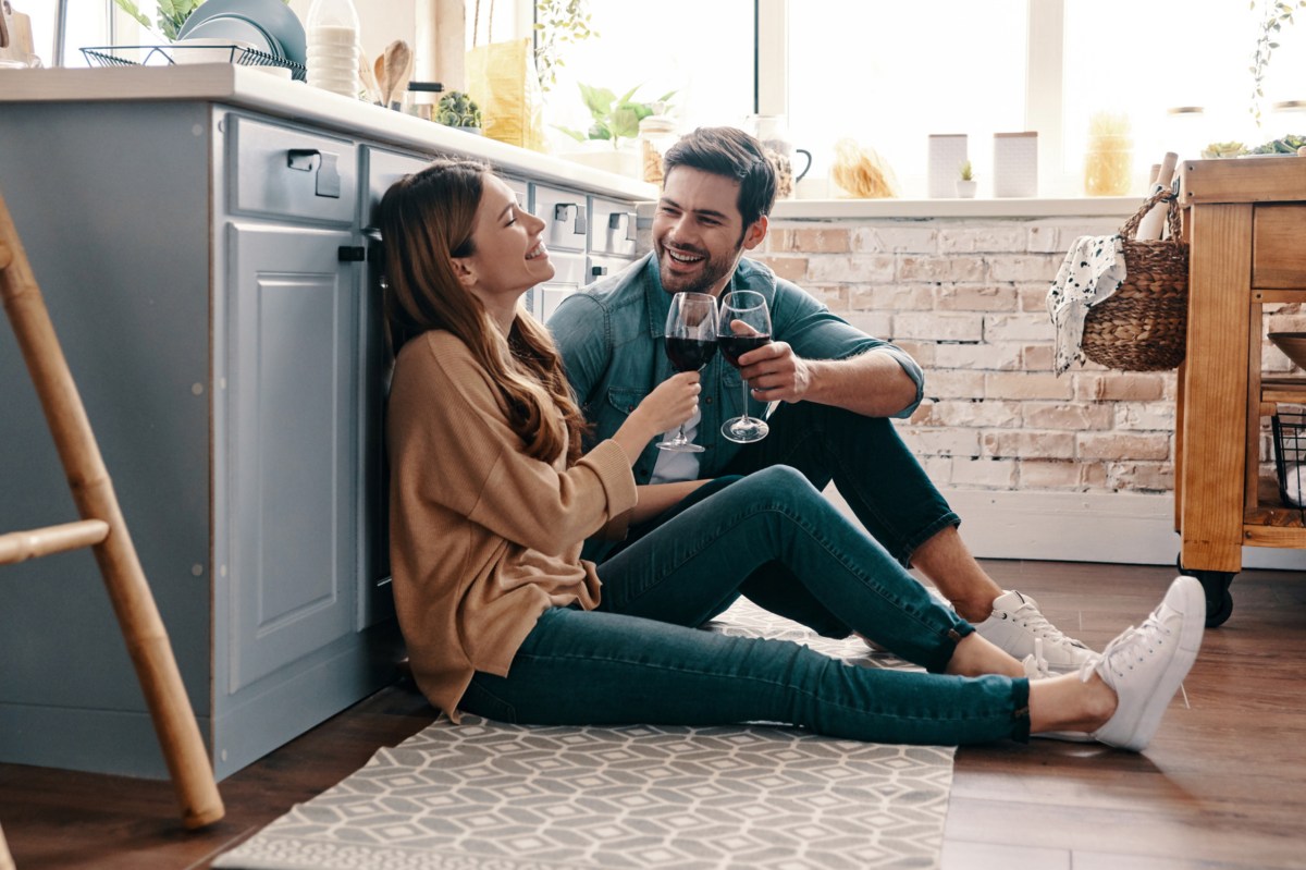 Frau und Mann sitzen in der Küche auf dem Boden und trinken Wein.