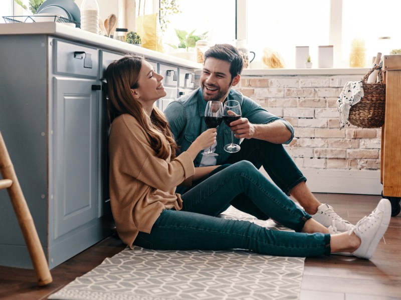 Frau und Mann sitzen in der Küche auf dem Boden und trinken Wein.
