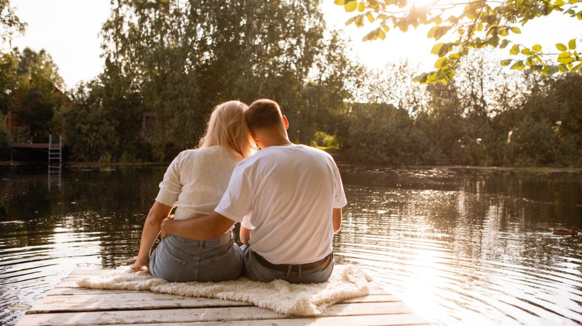 Mann und Frau auf Steg, die sich gegenseitig umarmen und auf den See blicken