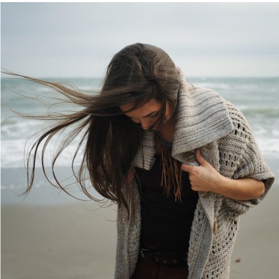 Frau am Strand mit dunklen Haaren die im Wind wehen, die mit dem Gesicht nach unten schaut