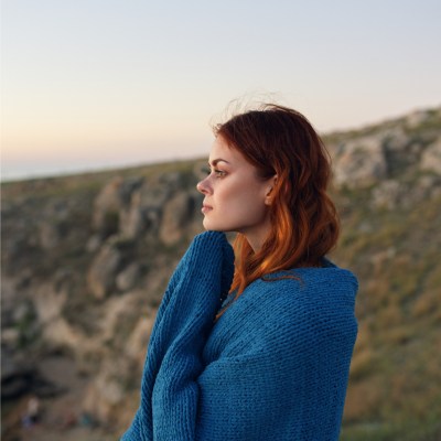Frau mit roten Haaren am Strand, die zur Seite schaut und den Sonnenuntergang anschaut