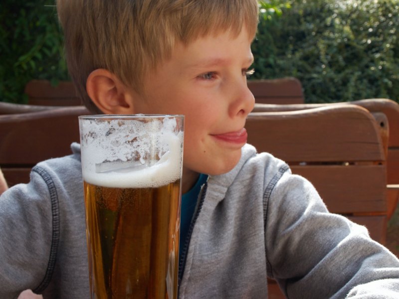 Etwa 10-jähriger Junge sitzt vor einem großen Glas Bier.
