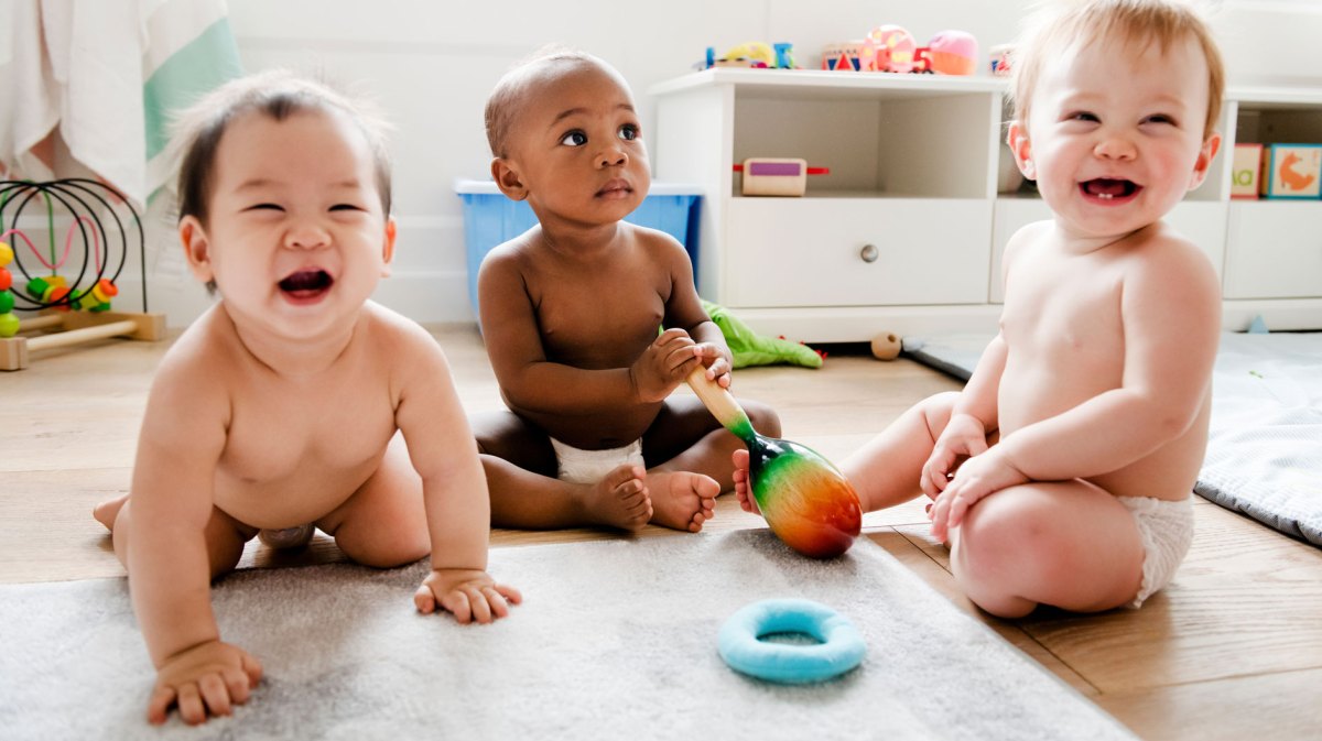 Drei Babys spielen nur in Windeln bekleidet in einem Kinderzimmer.