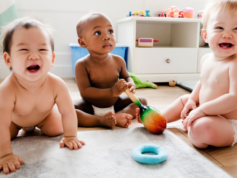 Drei Babys spielen nur in Windeln bekleidet in einem Kinderzimmer.