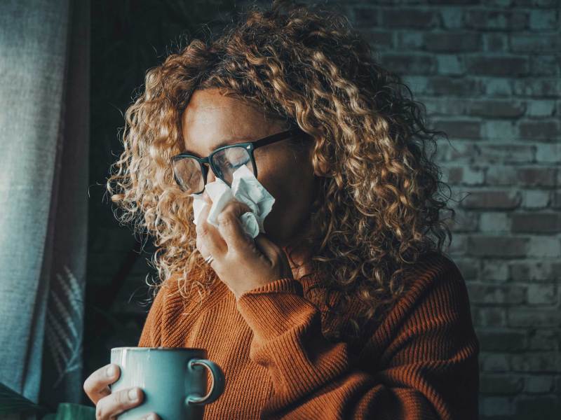 Erkältete Frau mit verstopfter Nase hält Taschentuch.