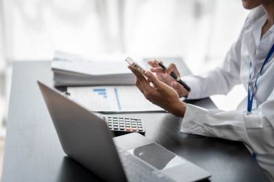 Frau sitzt am Laptop und tippt auf ihrem Handy.