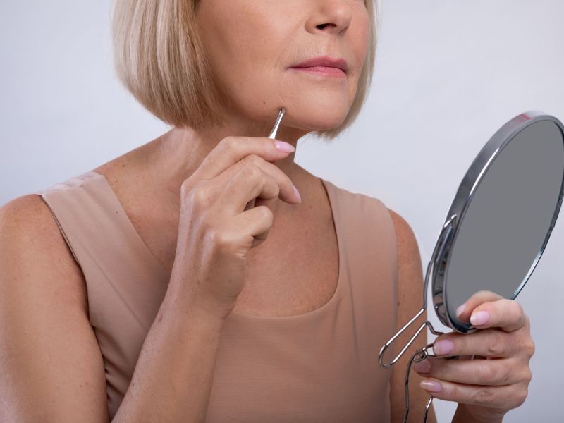 Frau entfernt sich Gesichtshaare mit Pinzette vor Spiegel