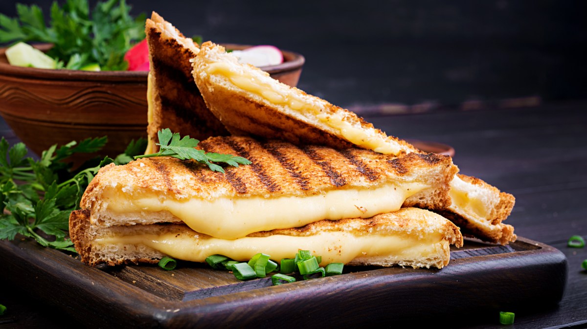 Gegrillte Käsesandwiches auf einem schwarzen Teller. Dazu Salat.