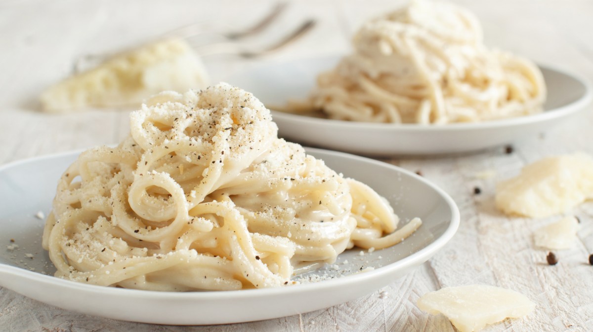 Spagetthi mit Käse und Parmesan serviert auf einem Tisch neben einem Stück Parmesan