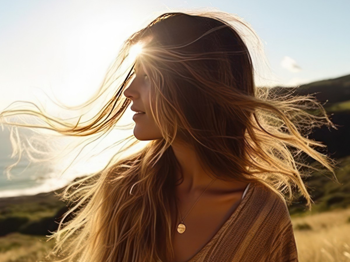 Frau im Sonnenschein, die ihre Haare zur Seite schwingt, während sie auf einer Wiese steht