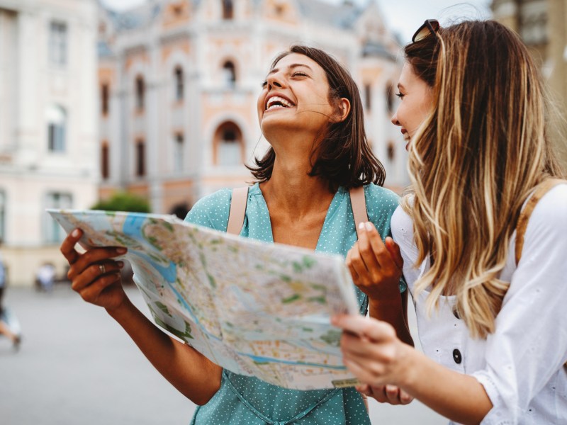 Zwei Frauen schauen gemeinsam auf eine Landkarte, lachen dabei