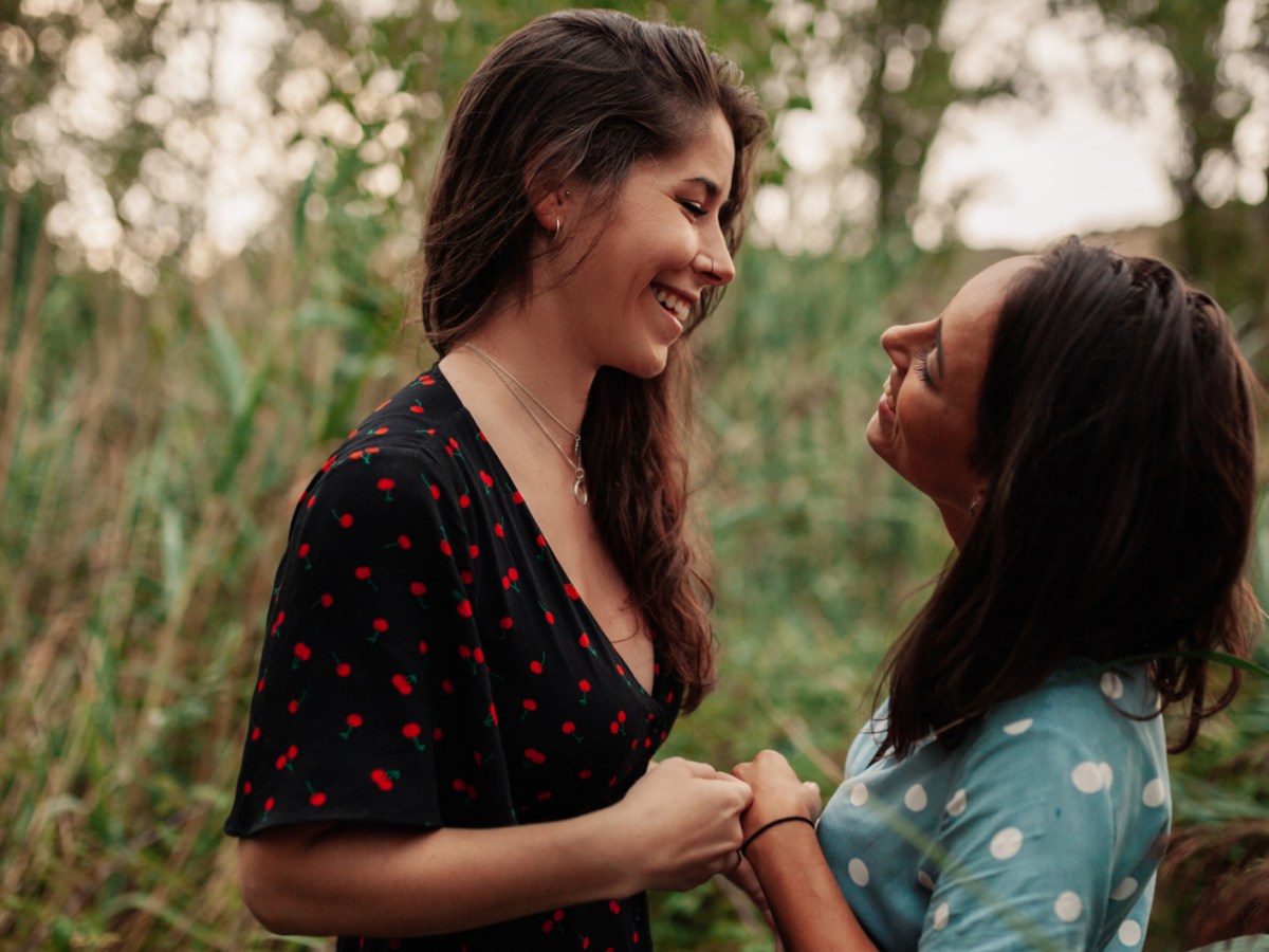 Zwei Frauen in einer Gartenlandschaft, die sich verliebt anschauen und Hände halten