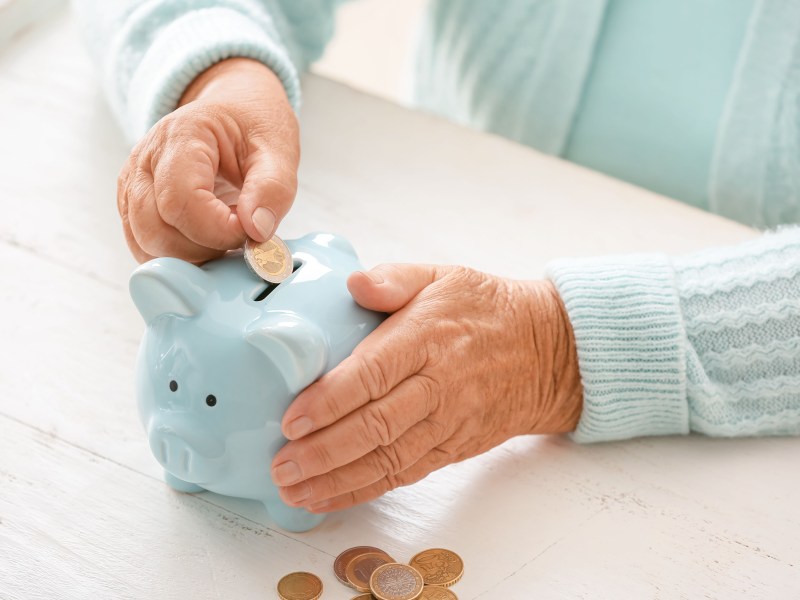 Ältere Frau wirft Geld in ein Sparschwein.