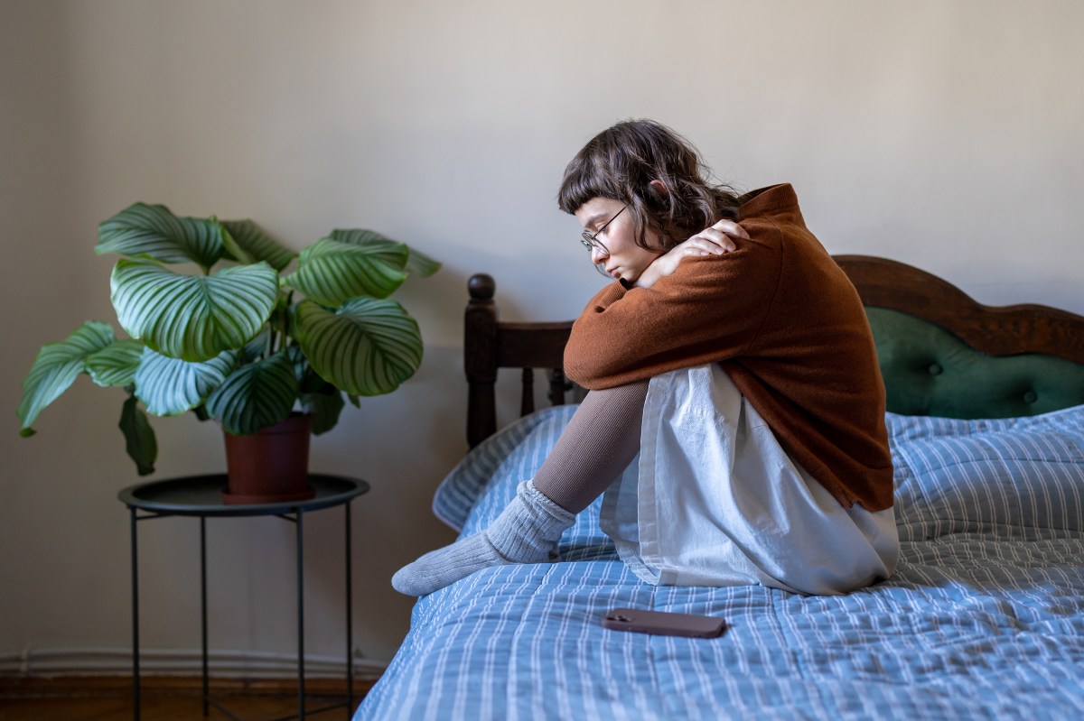Verärgertes, depressives Teenager-Mädchen sitzt auf dem Bett neben dem Smartphone, fühlt sich einsam und frustriert.