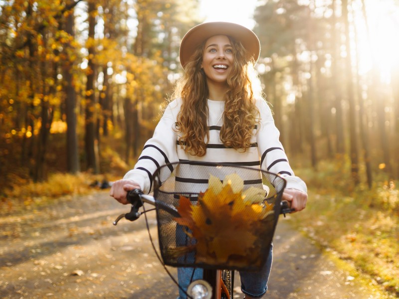 Frau mit Hut fährt auf einem Fahrrad, durch den herbstlichen Wald.