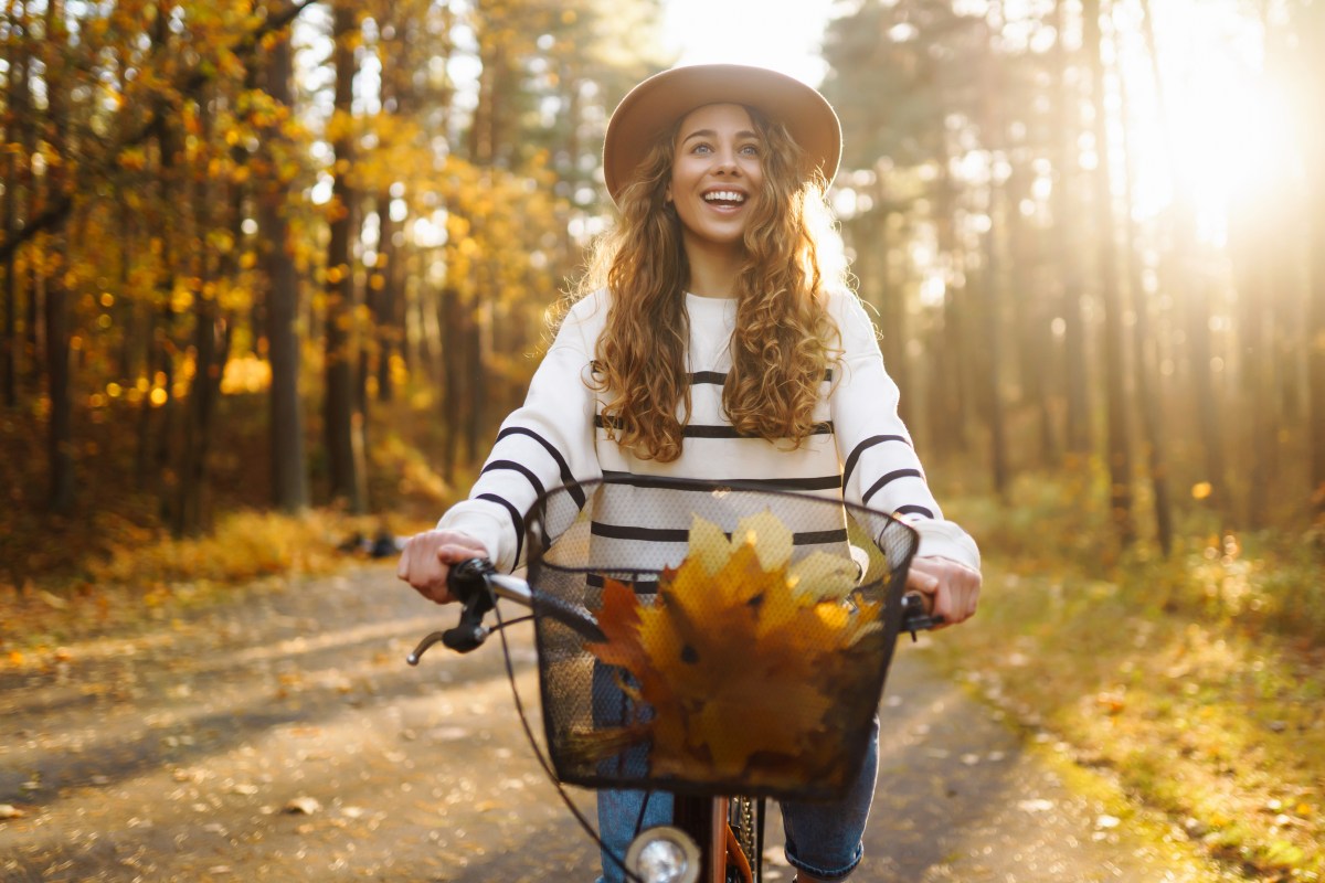 Frau mit Hut fährt auf einem Fahrrad, durch den herbstlichen Wald.