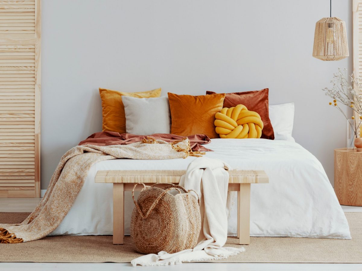 Bett dekoriert mit Kissen, einer Tagesdecke und einer Bank am Fußende