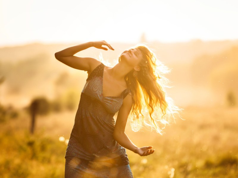 Frau tanzt in einem Feld bei untergehender Sonne.
