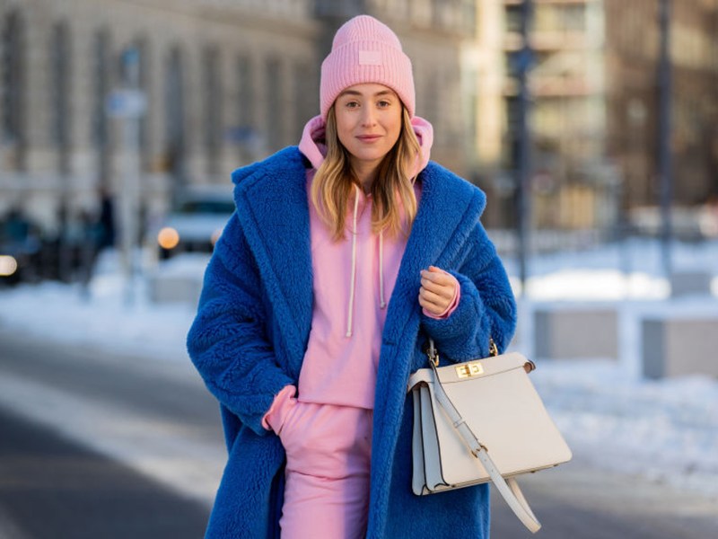 Frau trägt ein Winter-Outfit mit Mütze, Mantel und Swetpants.