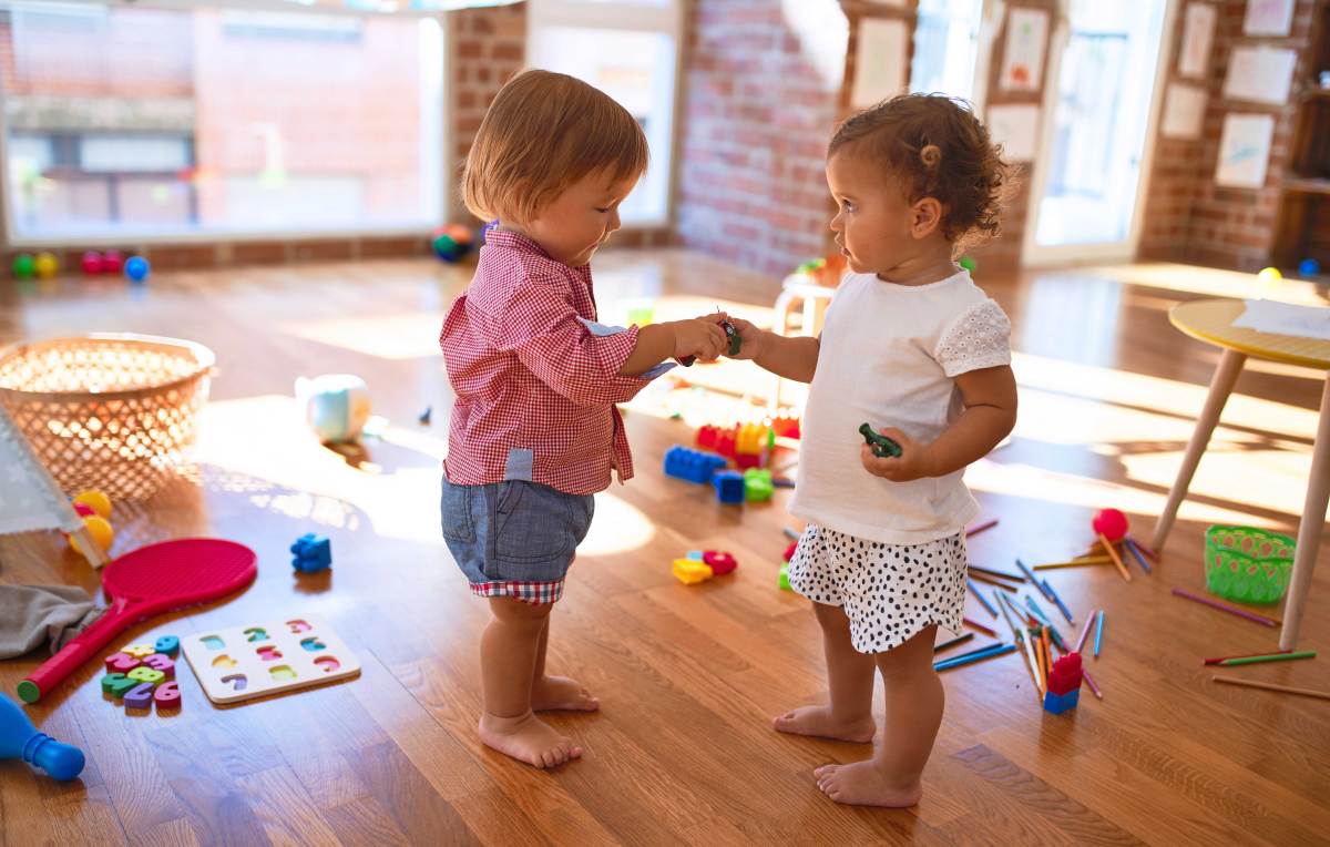 Zwei kleine Kinder spielen inmitten von viel Spielzeug im Kindergarten.