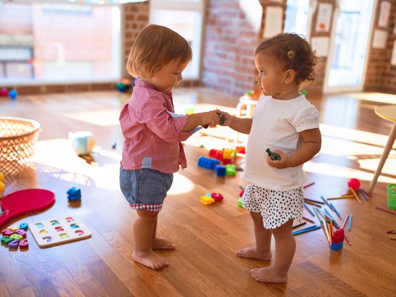 Zwei kleine Kinder spielen inmitten von viel Spielzeug im Kindergarten.