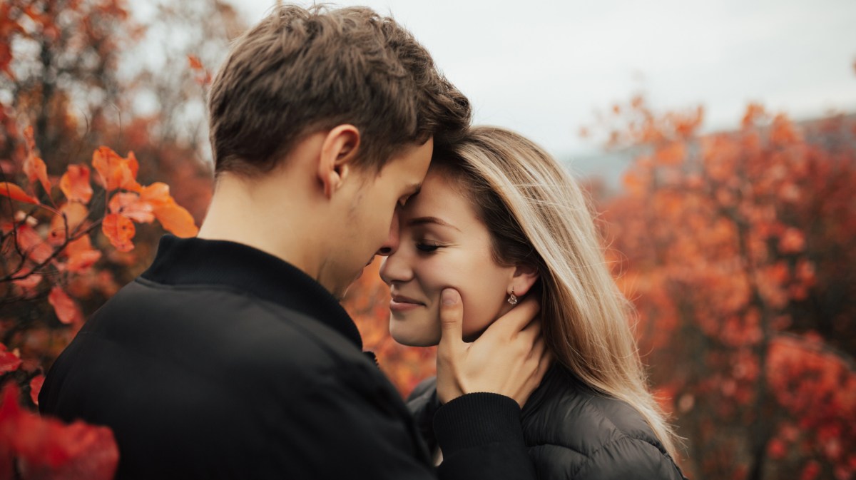 Mann küsst Frau auf die Stirn zwischen herbstlichen Bäumen