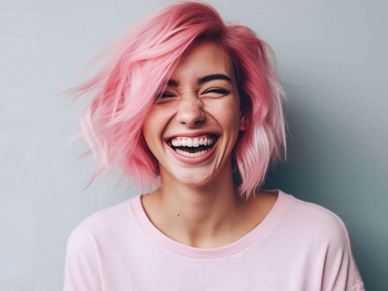 Frau mit rosa Haaren lacht vor Freude in die Kamera.