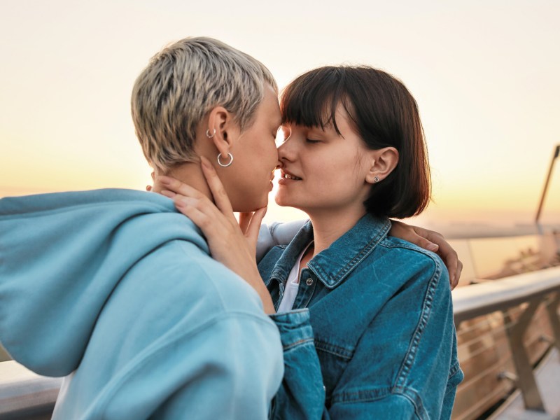 Lesbisches Paar, das auf einer Promenade steht und kurz davor ist, sich zu küssen im Sonnenuntergang