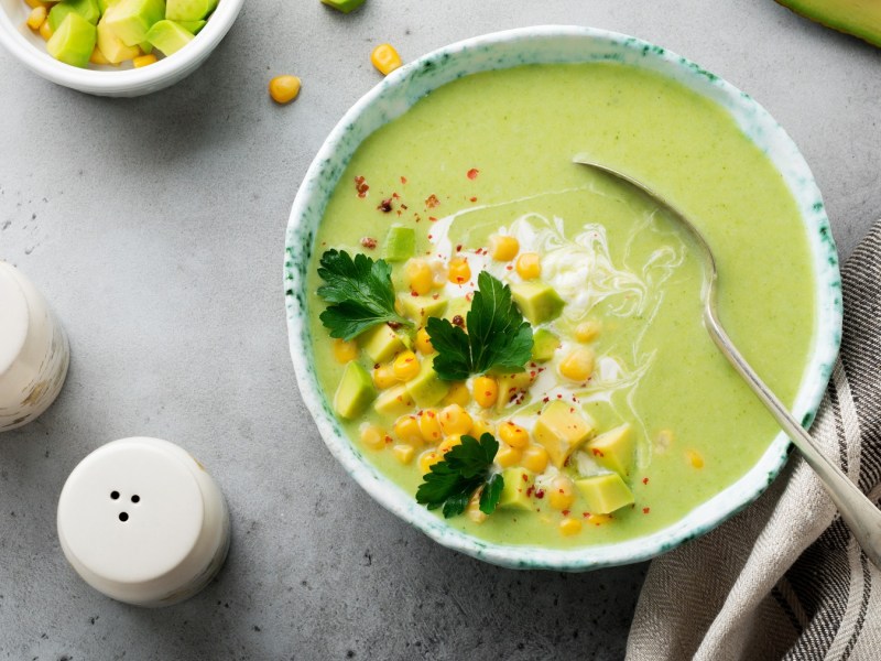 Eine weiße Schale mit der hellgrünen Suppe auf einem grauen Tisch. Alles direkt von oben fotografiert.