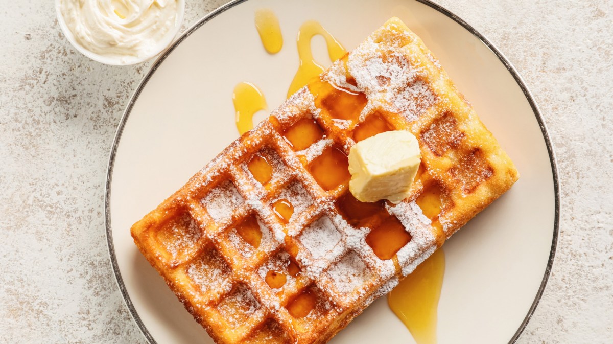 Belgische Waffel auf weißem Teller mit Sirup, Puderzucker und ein Stückchen Butter.