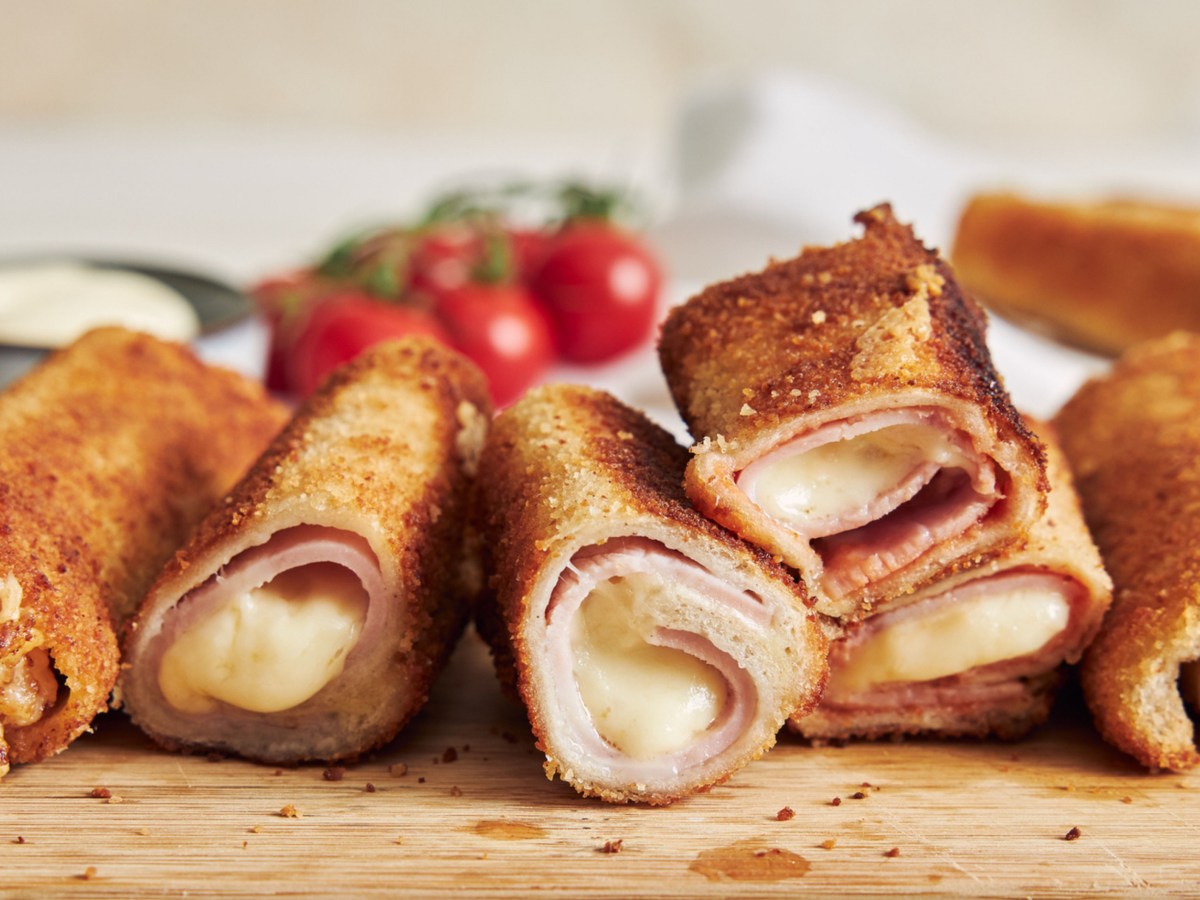 Toaströllchen mit Schinken und Käse auf Holzbrett.