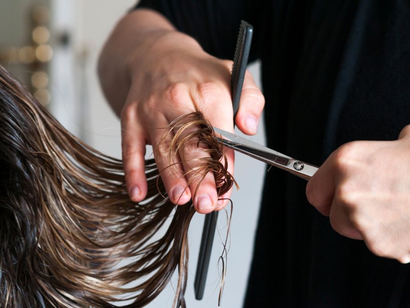 Frisörin, die einer Frau die langen Haare abschneidet.