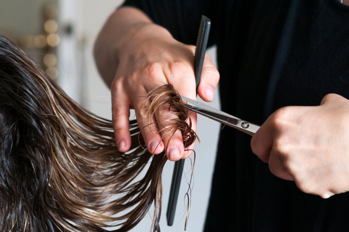 Frisörin, die einer Frau die langen Haare abschneidet.