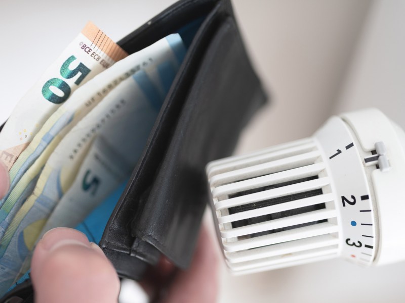 Jemand hält sein Portemmonaie neben das Heizungsthermostat. und