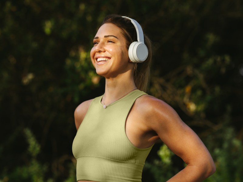 Frau im Sport-BH, die Kopfhörer aufhat, lächelt und im Wald steht