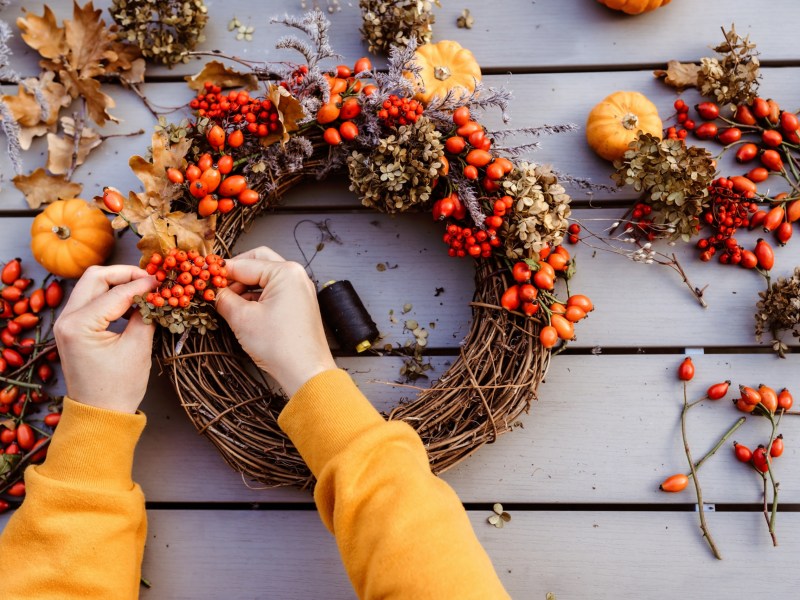 Eine Frau bastelt einen Herbstkranz mit Hagebutten und kleinen Kürbissen.