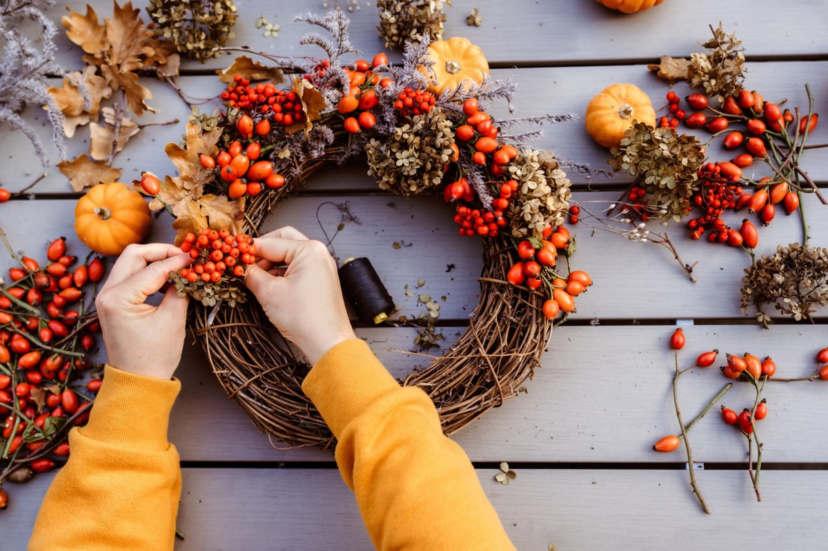 Eine Frau bastelt einen Herbstkranz mit Hagebutten und kleinen Kürbissen.