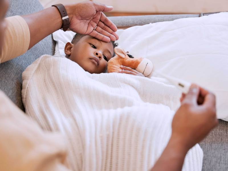 Mutter legt ihrem kranken Sohn die Hand auf die Stirn, in der anderen hält sie ein Fieberthermometer.
