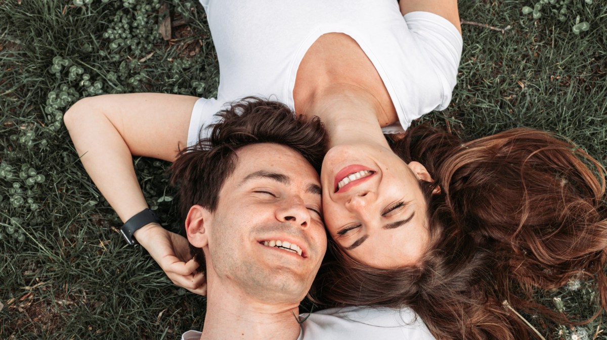 Frau und Mann, die verliebt auf dem Rasen liegen und lachen