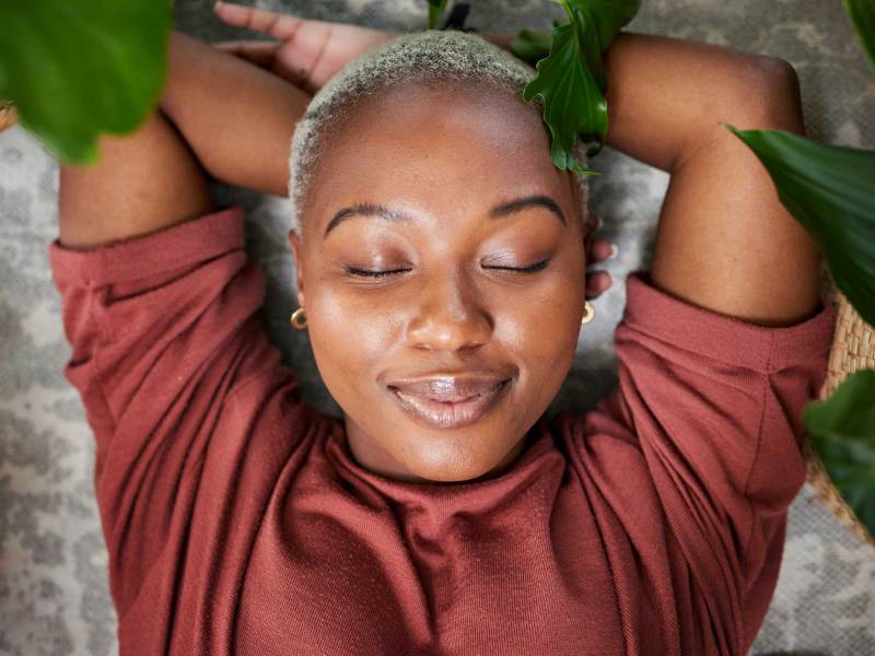 Zufriedenes Gesicht einer weiblichen Person auf dem Boden liegend umgeben von Zimmerpflanzen