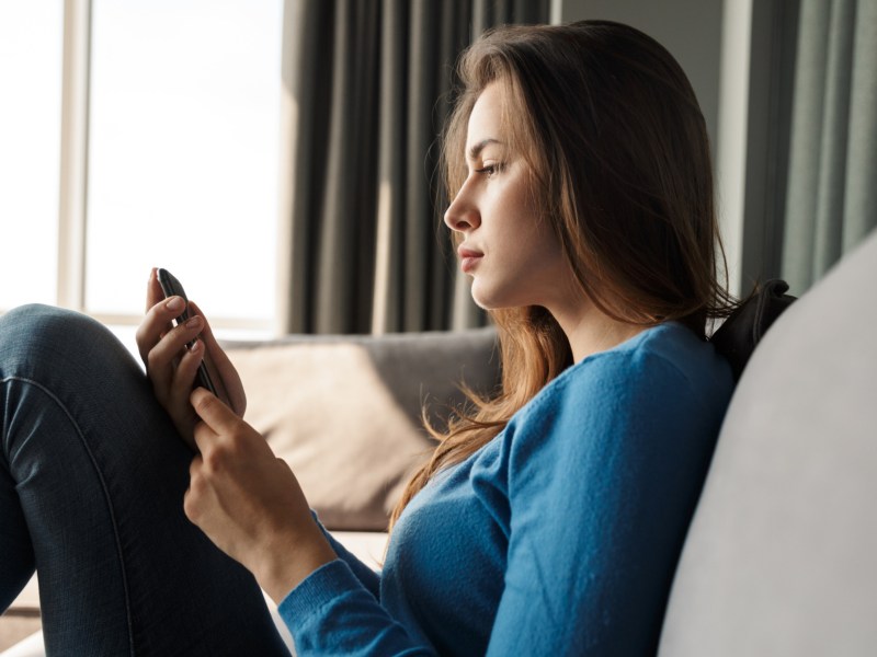 Frau auf dem Sofa, die skeptisch auf ihr Handy schaut