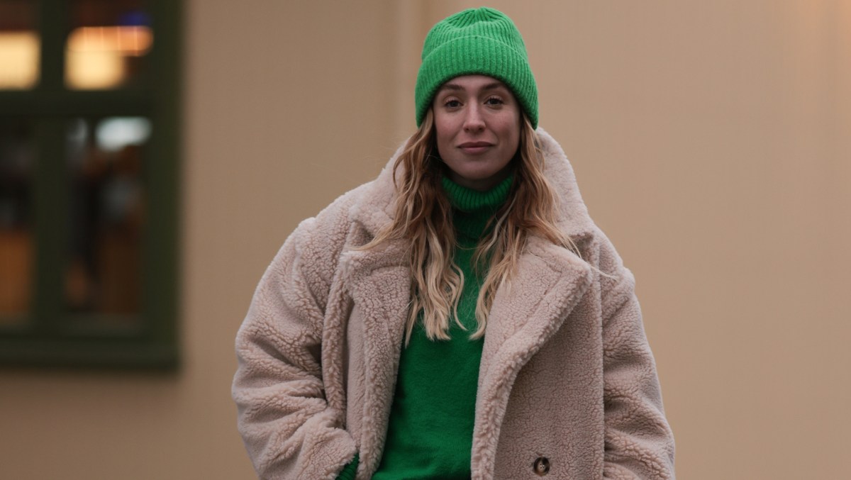 Frau trägt einen Teddyfell-Mantel und eine grüne Mütze.
