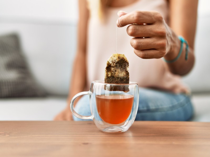 Eine Frau zieht einen Teebeutel aus einer Teetasse.