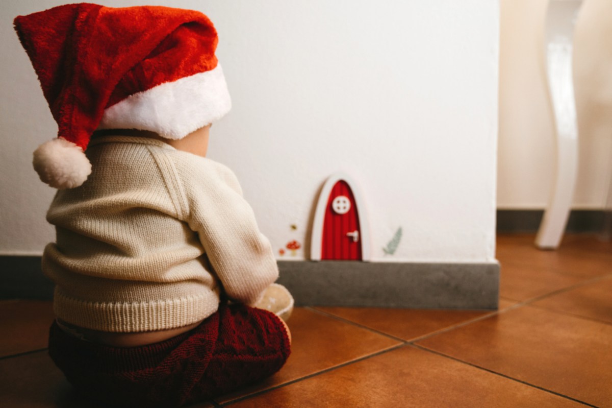 Ein kleines Kind sitzt auf dem Boden vor einer roten Wichteltür.
