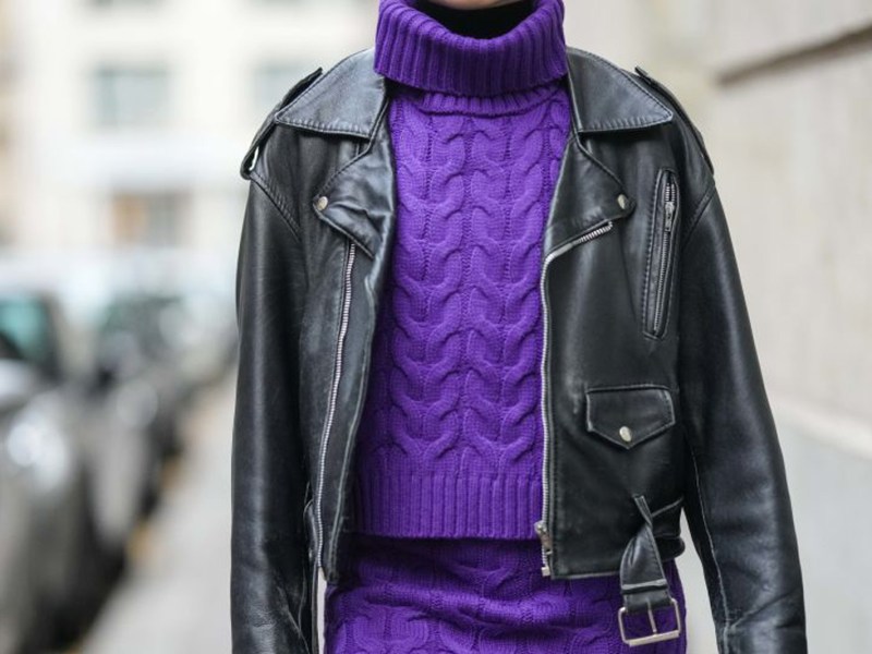 Frau trägt eine Lederjacke und einen lilafarbenen Zopfstrickpullover.