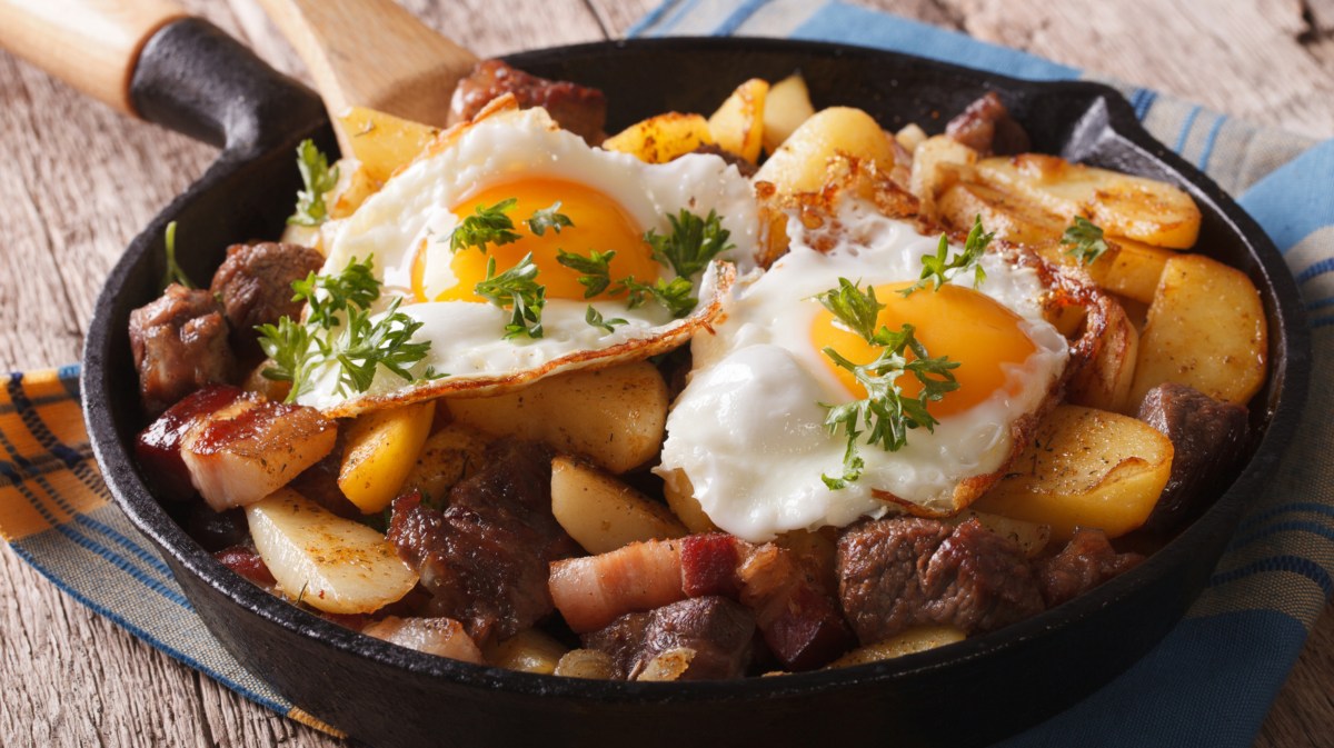 Bauernschmaus mit Kartoffeln, Wurst und Spiegeleier in einer Pfanne.