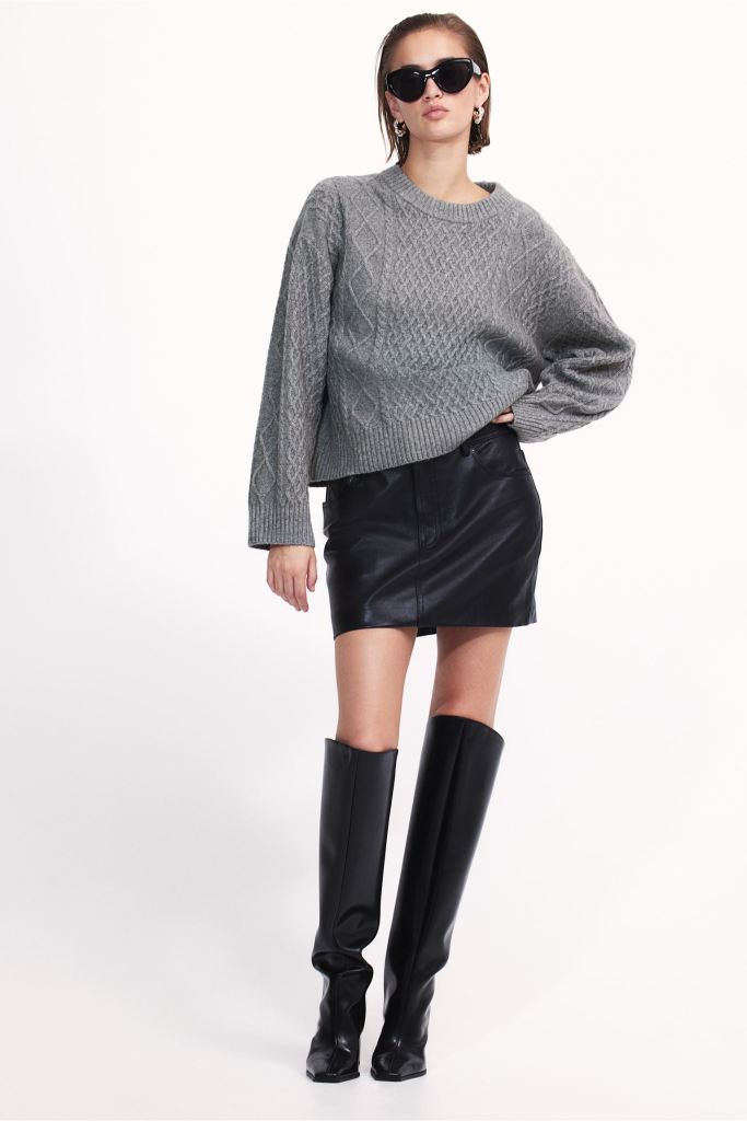 H&M Model trägt Zopfstrick-Pullover mit Mini-Rock und Stiefeln.